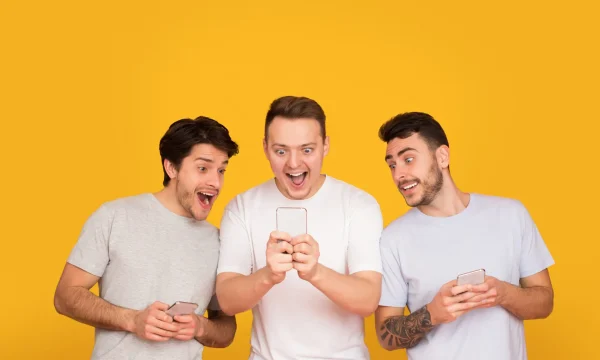 Surprised friends holding mobile phones, reading good news over orange background
